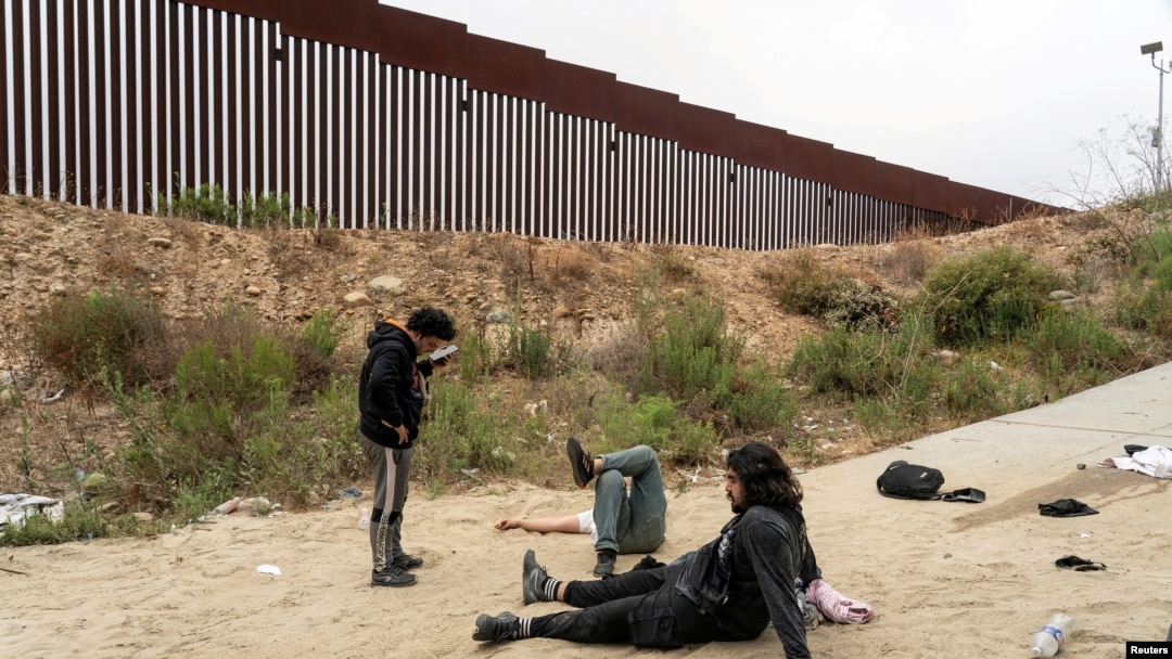 Asylum-seeking migrants from Turkey lay on the ground as they suffer from leg injuries after jumping down from the top of the border wall to cross into the U.S. from Mexico as seen from Tijuana, Mexico, June 8, 2024. 