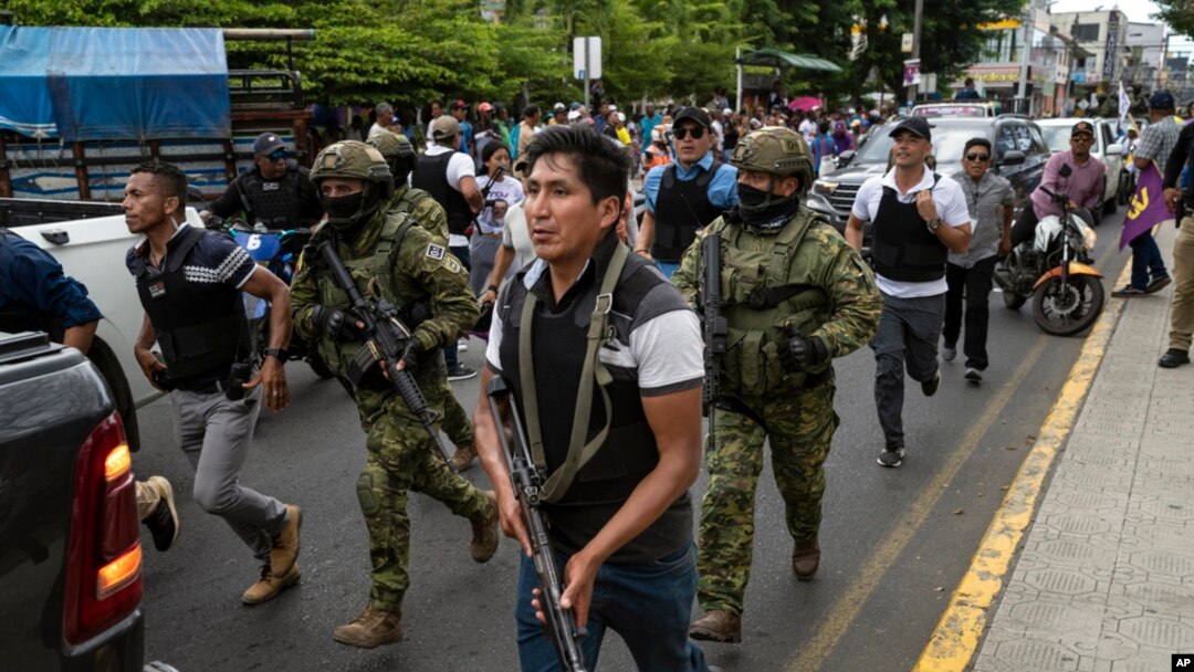 Soldiers and police provide security behind an armored vehicle as supporters of presidential candidate Daniel Noboa, of the National Democratic Action Alliance political party, attend a rally with their candidate in downtown Esmeraldas, Ecuador, Oct. 6, 2023. 