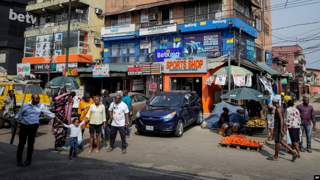 People walk past sports betting shops on a street in Lagos, Nigeria, Monday, Dec. 5, 2022. (AP Photo/Sunday Alamba)