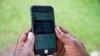 FILE - A woman scrolls through her social media account on her phone in Kampala, July 5, 2018. Uganda's Communications Commission issued a notice this week requiring anyone wishing to publish information online to first be licensed.