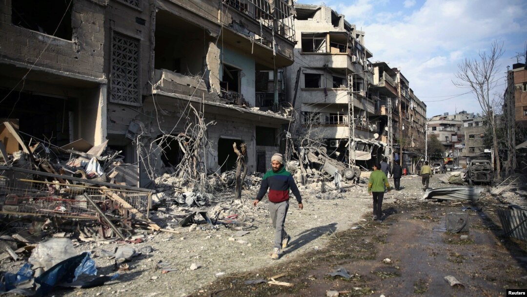 People walk past bombed-out buildings after an air raid in the besieged town of Douma, east of Damascus, Syria, Feb. 23, 2018.