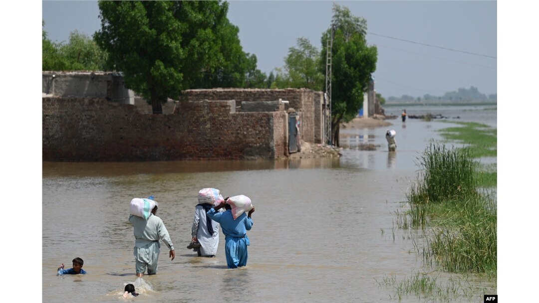 Flood-affected people wade through a flooded area with relief food bags as they return to their homes on the outskirts of Jacobabad, Sindh province, Sept. 6, 2022.