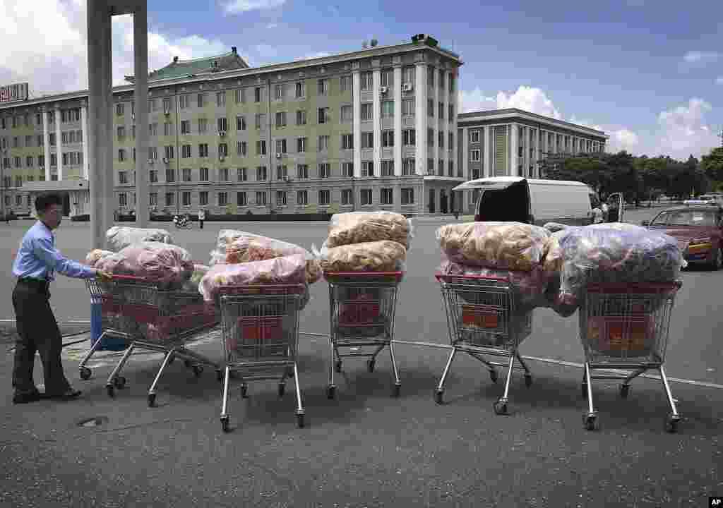A man waits with shopping carts at a parking lot in front of a department store in Pyongyang, North Korea.