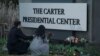 FILE - A woman holds flowers in front of a sign for The Carter Presidential Center after the death of former U.S. President Jimmy Carter at the age of 100 in Atlanta, Georgia, Dec. 29, 2024. 
