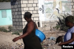 People walk past an Oxfam sign in Corail, a camp for people displaced by the 2010 earthquake, on the outskirts of Port-au-Prince, Haiti, Feb. 16, 2018.