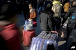 A woman with her luggage waits as Chinese passengers arrive at the Beijing railway station to catch trains in Beijing, Jan. 31, 2016.