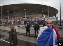 A French supporter wrapped in his national flag passes by police officers guarding the Stade de France stadium prior to the international exhibition soccer match between France and Russia in Saint Denis, north of Paris, March 29, 2016.