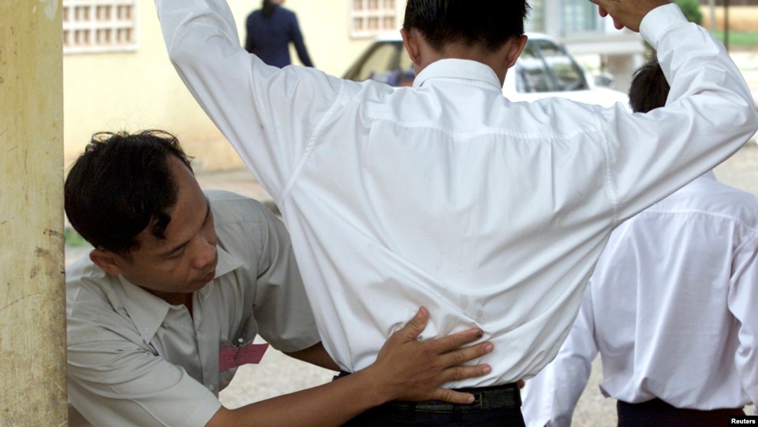 FILE - A Cambodian school security official searches a student for exam 'cheat sheets' at the gates of a school in Phnom Penh.