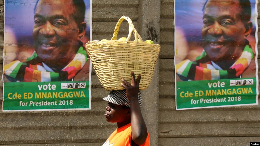 FILE - A street vendor carries fruit while passing campaign posters of President Emmerson Mnangagwa's ruling ZANU-PF party, in Mutare, Zimbabwe, May 19, 2018. 