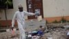 FILE - A man picks up an item belonging to a student at the site of a bomb blast in the university town of Zaria, Nigeria, July 7, 2015.