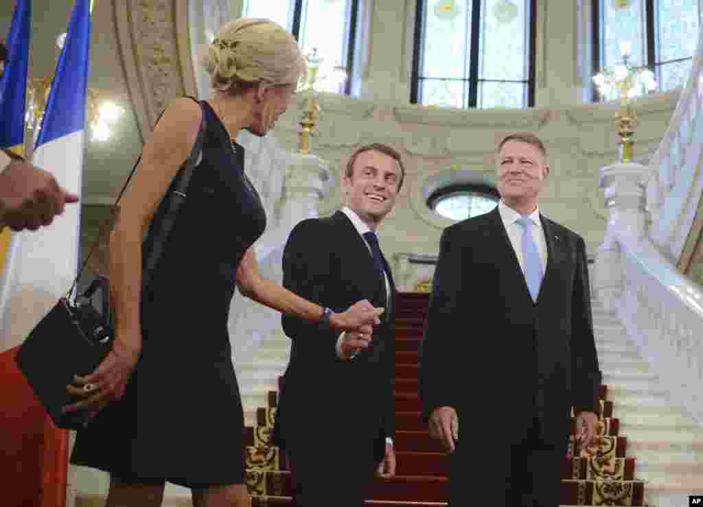 French President Emmanuel Macron,center, holds his wife Brigitte's hand, as Romanian counterpart Klaus Iohannis smiles, in Bucharest, Romania.