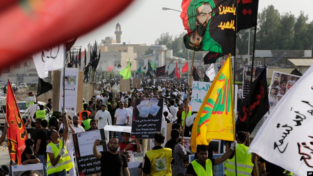 Saudis marching in a funeral procession carry religious flags and signs blaming the fundamentalist Wahhabi stream of Sunni Islam's ideology for recent suicide attacks on Shi'ite mosques in the kingdom, May 30, 2015, in Tarut, Saudi Arabia.