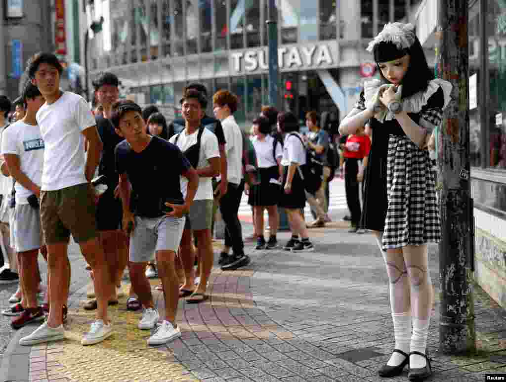Pedestrians look at "doll" model Lulu Hashimoto standing on the street in Tokyo, Japan, Aug. 23, 2017.