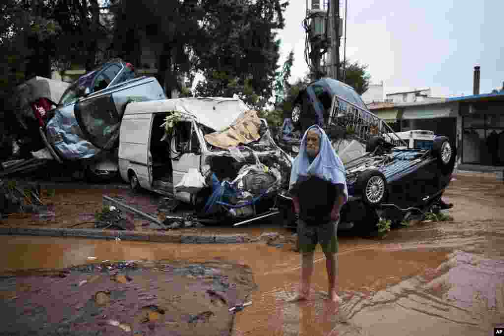 A barefoot man stands in front of a pile of vehicles in the municipality of Madra western Athens, Greece. Flash floods in the Greek capital&#39;s western outskirts turned roads into raging torrents of mud and debris, killing at least nine people, inundating homes and businesses and knocking out a section of a highway.