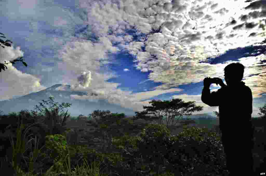 A man takes a photo as a puff of smoke comes from Mount Agung volcano, taken from the Rendang sub-district in Karangasem Regency on Indonesia&#39;s resort island of Bali.