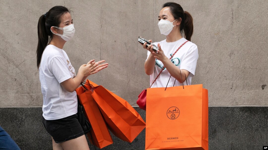 Women carrying Hermes shopping bags use hand sanitizer as they walk on Wall Street, July 30, 2020, in New York.