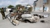 FILE - Somali soldiers stand near the wreckage of car bomb that was detonated at the main gate of the presidential palace in Mogadishu, July, 9, 2014.