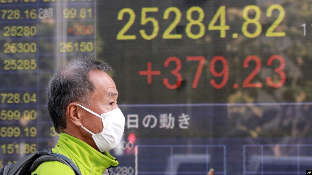 FILE - A man walks by an electronic stock board of a securities firm in Tokyo, November 11, 2020.