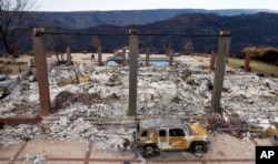 FILE - A vehicle rests in front of a home leveled by the Camp Fire in Paradise, Calif., Dec. 3, 2018. Authorities estimate it will cost at least $3 billion to clear debris of 19,000 homes destroyed by California wildfires last month.