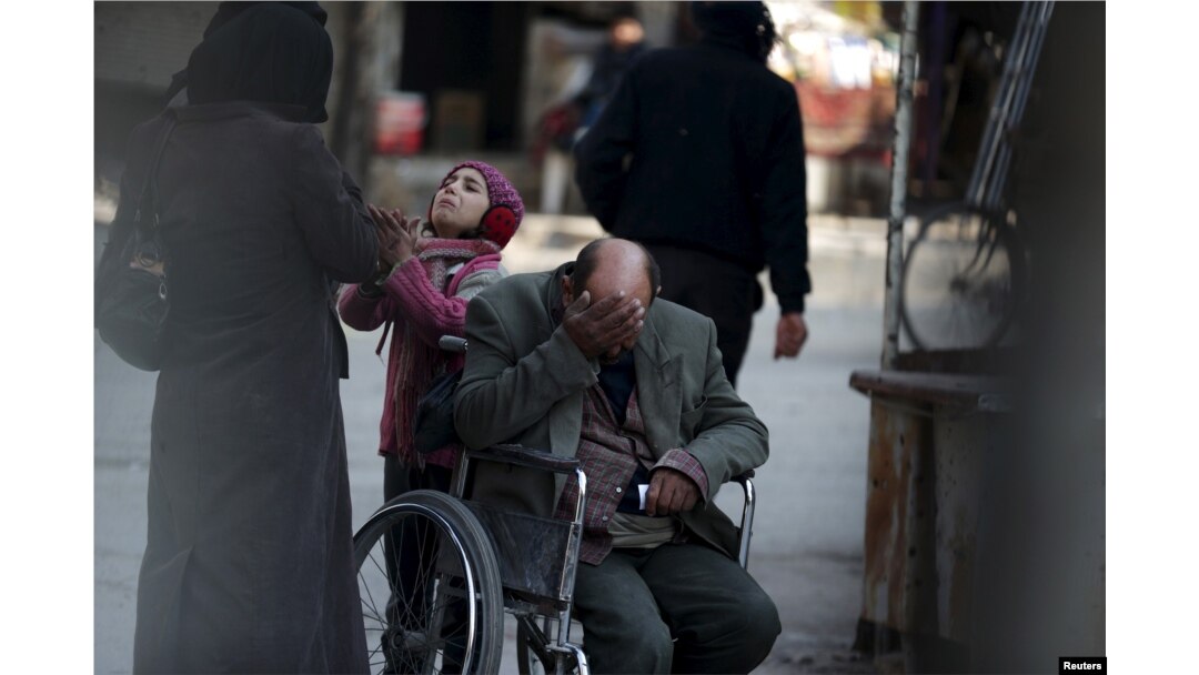 A girl with her father in a wheelchair asks for help from passers-by to pay a medical bill, in Douma, Syria, Feb. 3, 2016.
