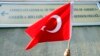 FILE - A person holds a Turkish flag under a sign on the U.S. Consulate in Istanbul.