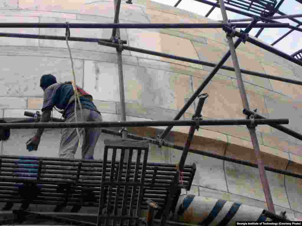 A worker cleans a portion of the Taj Mahal complex. Marble on the right shows brownish discoloration caused by particles of carbon, and dust.