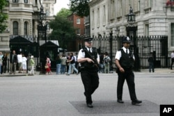 FILE - Armed police officers cross the road outside the security gates at Downing Street in London, Aug 16, 2006.
