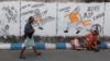 FILE - A man walks past a woman who sits by a wall with graffiti that mocks Indian politicians ahead of the general election in Kolkata, India, Apr. 1, 2019.