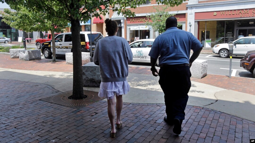 FILE - A woman who voluntarily went to the police for help kicking her heroin addiction walks from the police station for her ride to an area detox facility, in Gloucester, Massachusetts, July 10, 2015.