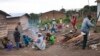 FILE - A man cuts wood as women prepare a meal in the camp for Central African refugees in Garoua Boulai, on the Cameroonian side of the border with the Central African Republic, April 28, 2014.