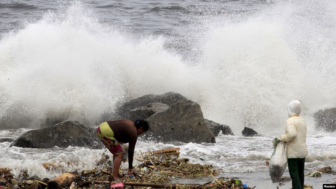 FILE - Residents collect recyclable materials from floating garbage found in the sea, while big waves crash along the coastline due to strong winds brought by Typhoon Goni, locally named as Ineng, at Manila bay, Aug. 22, 2015.