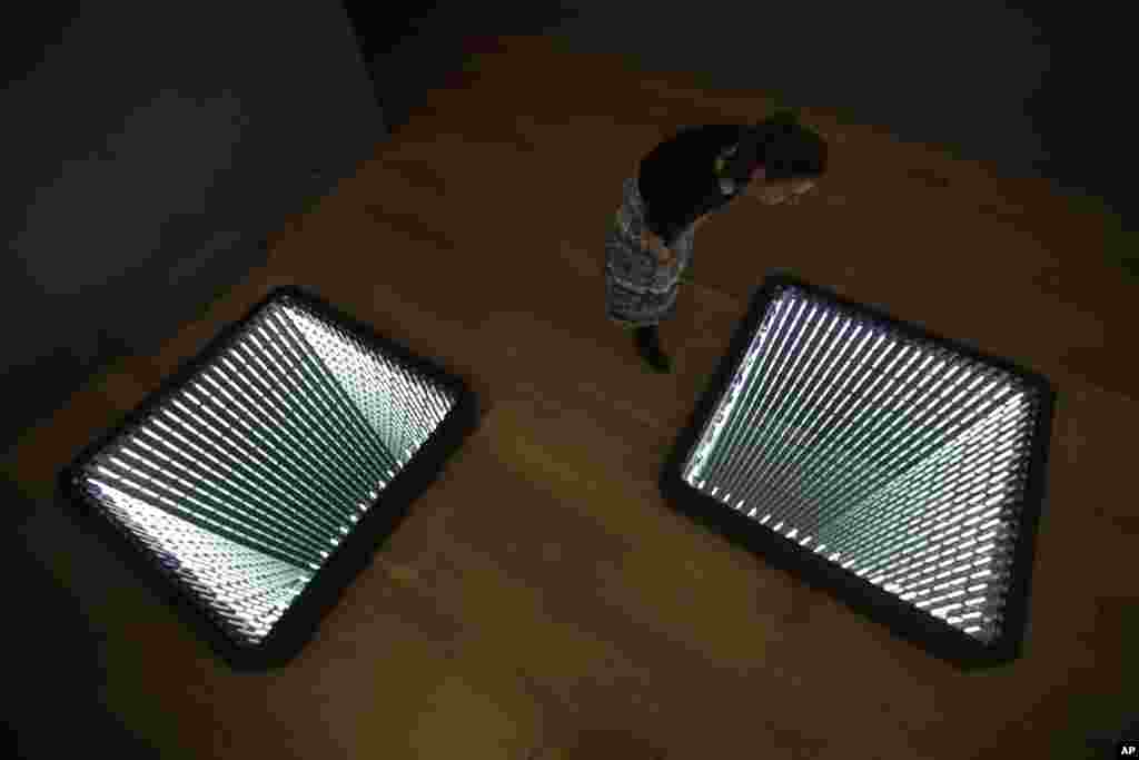 A staff member poses for photographs looking at Chilean-born artist Ivan Navarro&#39;s two light box and mirror installation &quot;The Twin Towers&quot; during the media preview for the &quot;Age of Terror: Art since 9/11&quot; exhibition at the Imperial War Museum in London.