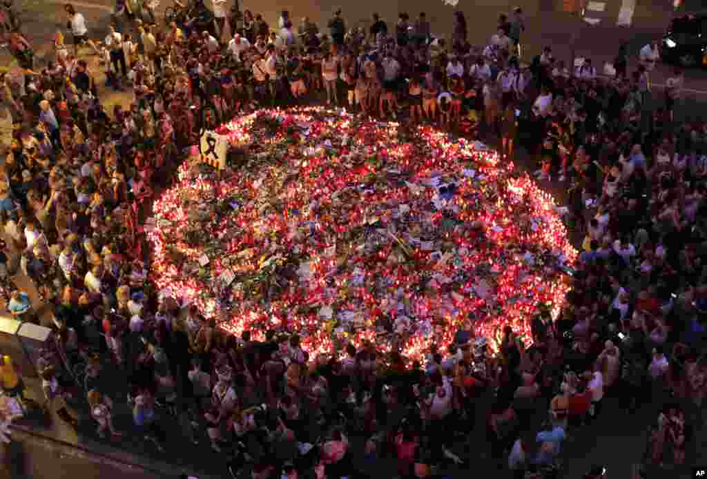 People pay respects at a memorial tribute of flowers, messages and candles to the victims on Barcelona's historic Las Ramblas promenade on the Joan Miro mosaic, embedded in the pavement where the van stopped after killing at least 14 people in Barcelona, Spain.