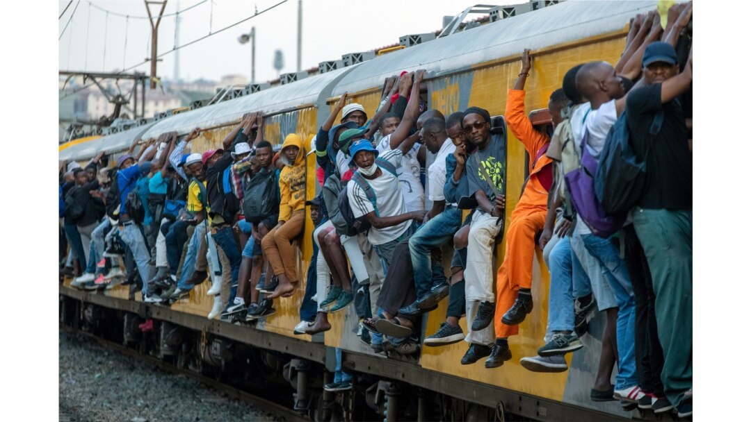 FILE - Train commuters hold on to the side of an overcrowded passenger train in Soweto, South Africa, March 16, 2020.