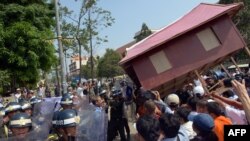 People carry a giant model of a house toward police as they protest government-sanctioned evictions, World Habitat Day, Phnom Penh, Oct. 10, 2013.