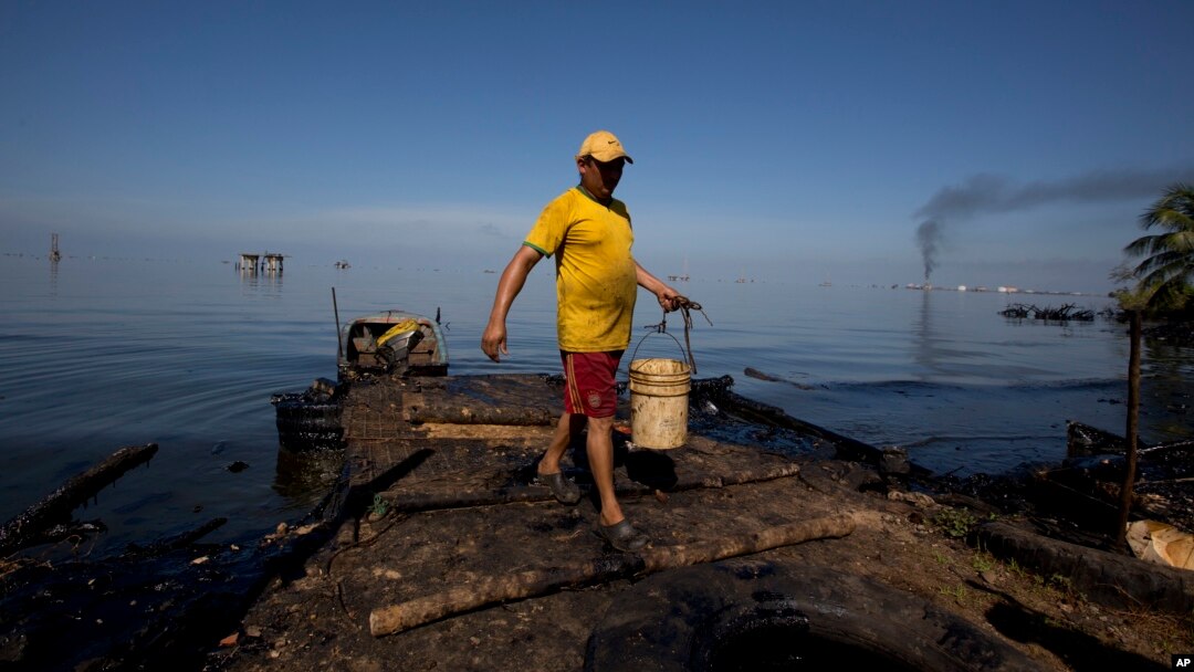 A fisherman collects water contaminated with oil from Maracaibo Lake in Cabimas, Venezuela, Aug. 20, 2018. The fisherman will use the water to clean fish. Broken down oil platforms span the vast lake, with downwind shores soaked in oil.