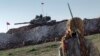 FILE - A Syrian Kurdish militia member of the YPG patrols near a Turkish army tank as Turks work to build a new Ottoman tomb in the background in Esme village in Aleppo province, Syria, Feb. 22, 2015.