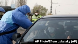 Фото: поліцейський в захисному костюмі заміряє температуру подорожуючому на в‘їзді до Києва, 16 квітня 2020 року