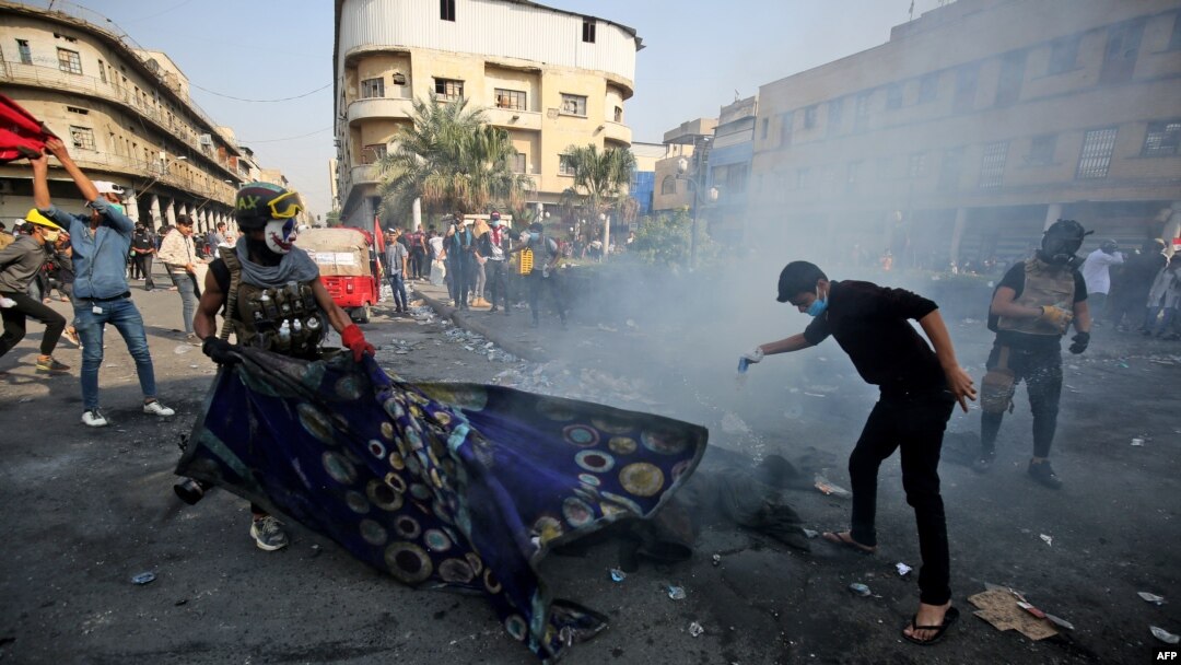 Iraqi demonstrators grapple with a tear gas canister during clashes with security forces in the capital Baghdad's al-Rasheed street near al-Ahrar bridge, Nov. 26, 2019.