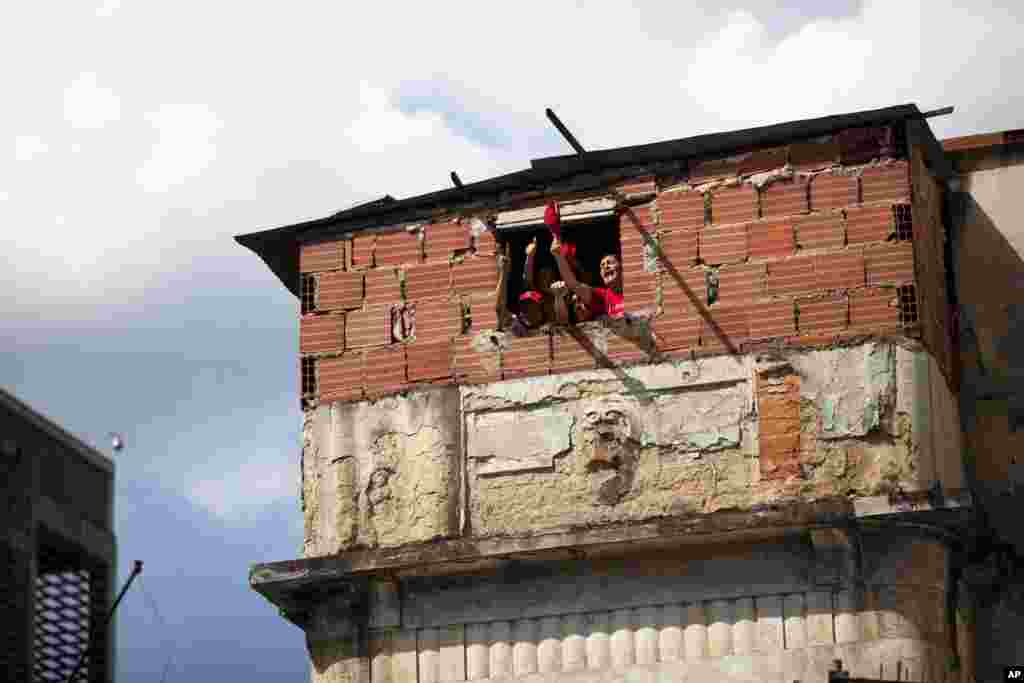 Pessoas dentro das suas casas cumprimentam membros de um colectivo pró-governo, que marcha pela baixa de Caracas, Fev. 20, 2014. 