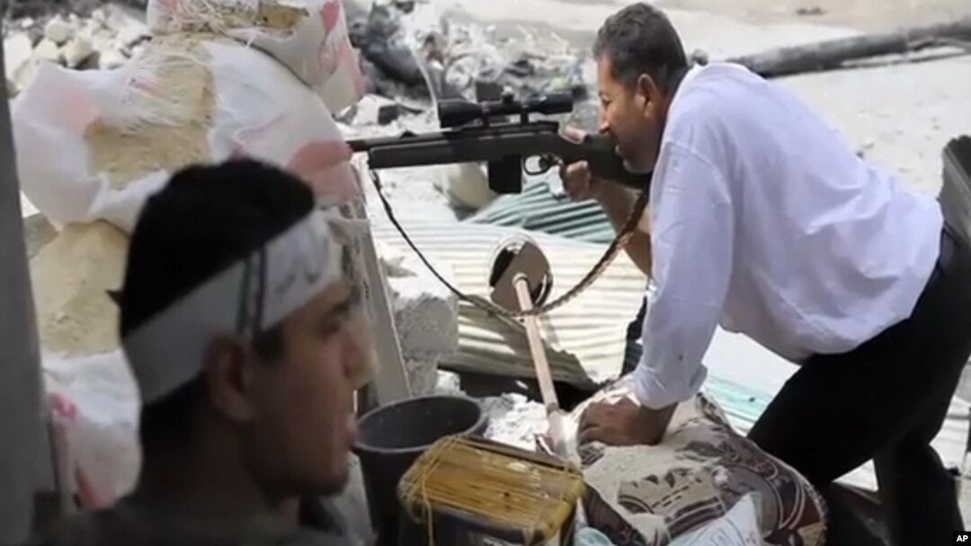 In this image made from video and accessed Saturday, Sept. 1, 2012, a Free Syrian Army fighter takes cover as another fighter fires at Syrian Army positions in Aleppo.