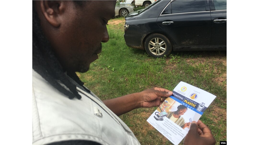 A man reading a Reserve Bank of Zimbabwe flyer promoting the use of plastic money to ease the country's over-a-year problem of cash shortages, Gokwe, Zimbabwe, Jan. 31, 2017. (S. Mhofu/VOA)