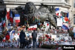 FILE - People look at flowers and other tributes to victims of last year's January and November shooting attacks near the statue at the Place de la Republique in Paris, France, January 6, 2016.