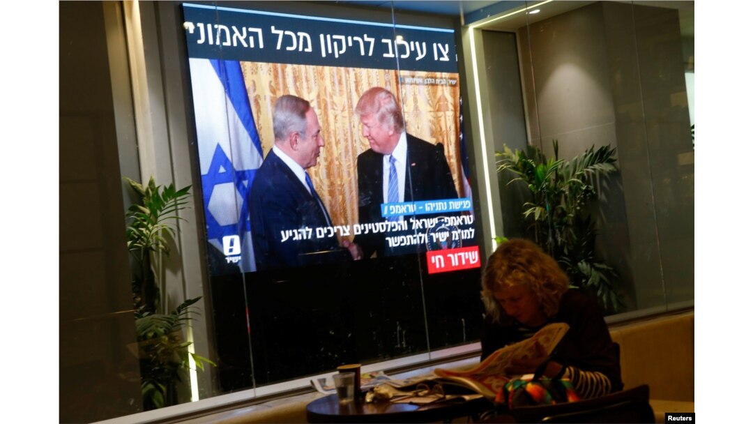 FILE - A woman reads a newspaper as monitors showing the meeting between U.S. President Donald Trump and Israeli Prime Minister Benjamin Netanyahu in Washington are seen next to a coffee shop in Tel Aviv, Israel, Feb. 15, 2017.