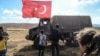 FILE - A man waves a Turkish national flag as a Turkish army vehicle drives past during a demonstration in support of the Turkish army's operation near the Turkey-Syria border near Reyhanli, Hatay, Oct. 10, 2017.
