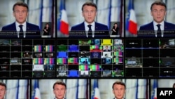 French President Emmanuel Macron is seen on screens as he delivers his televised New Year's address to the nation from the Elysee Palace in Paris on Dec. 31, 2024.
