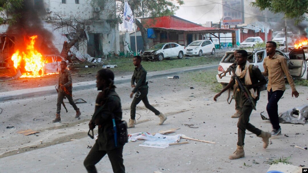 FILE - Security troops walk past burning cars after a fatal car bomb attack on a restaurant in Mogadishu, Somalia, May, 8, 2017. 