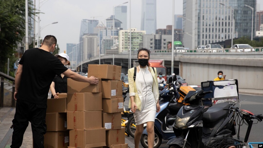 A woman wearing a mask walks past delivery workers moving boxes in Beijing on Aug. 20, 2020. U.S. and Chinese trade envoys discussed strengthening coordination of their government’s economic policies.
