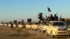 FILE - In this undated file photo released by a militant website, which has been verified and is consistent with other AP reporting, militants of the Islamic State group hold up their weapons and wave its flags on their vehicles in a convoy to Iraq, in Ra