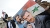 FILE - People wave Syrian flags and carry a poster depicting Syria's President Bashar al-Assad and Lebanon's Hezbollah Leader Sayyed Hassan Nasrallah during a rally to show support for al-Assad in Damascus, Syria.